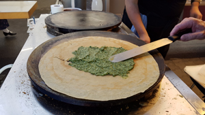 Eine frische Crêpe wird mit grüner Pesto bestrichen.
