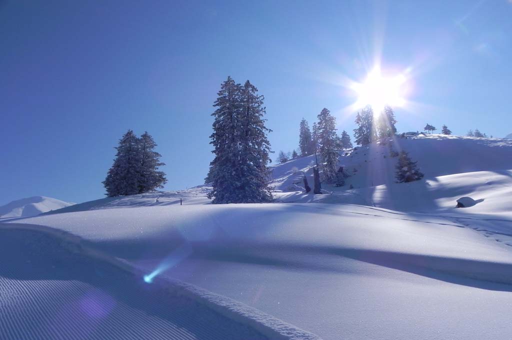 Winterliche Berglandschaft mit blauem Himmel und sternförmiger Sonne.