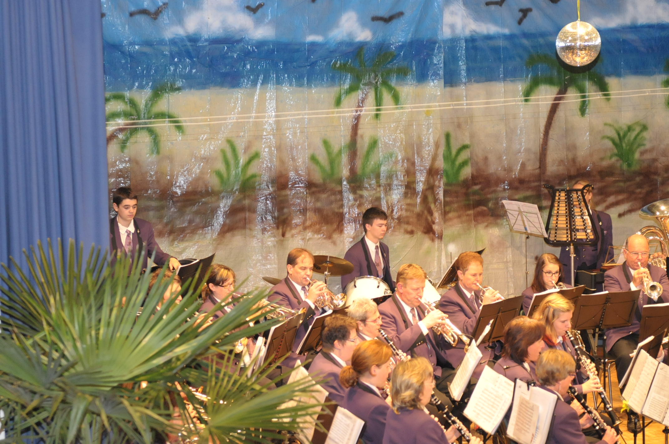 MGU auf der Bühne. Palmen im Hinter- und Vordergrund als Dekoration.