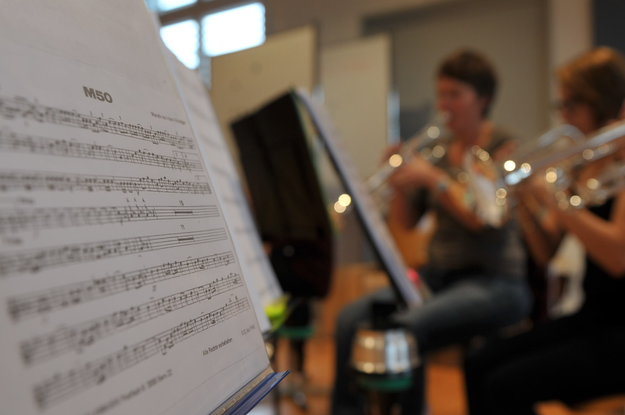 Noten auf Ständer. Verschwommen im Hintergrund zwei Trompentenspielerinnen.