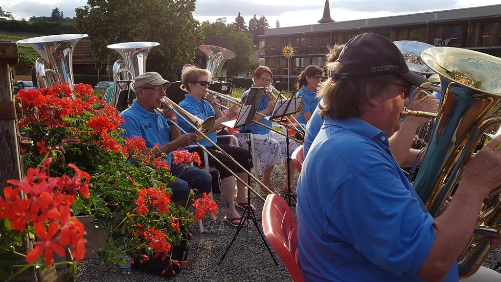 Links sind Geranien und auf dem restlichen Bild Musizierende. Am rechten Rand spielt Alfred Künzi Tenorhorn.