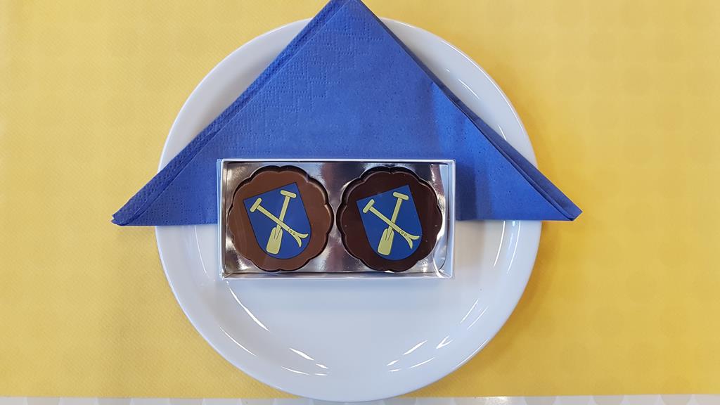 Schoggipräsent der Gemeinde. (Drappiert auf einem weissen Teller, auf welche in der oberen Hälfte eine zum Dreieck gefaltete blaue Serviette befindet. Das Teller steht auf einem gelben Tischset - also Uttigerfarben.