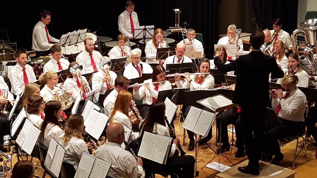 Eine Musikgesellschaft mit weissen Hemden und roten Kravatten auf der Bühne des Mehrzweckgebäudes.