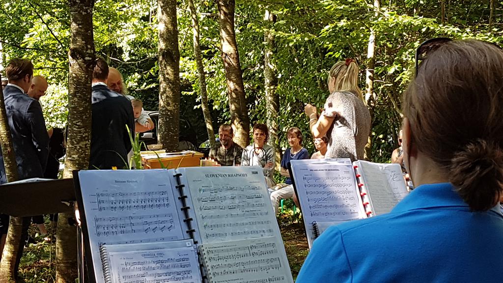 Blick über die Schulter einer Musikantin auf deren Notenständer. Im Hintergrund sind Bäume und Personen erkennbar.