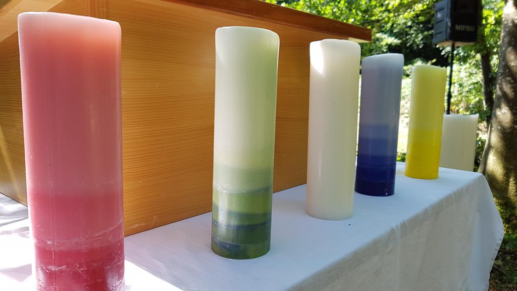 Fünf unterschiedlich farbige, dicke und grosse, Kerzen auf dem Tisch des Pfarrers.