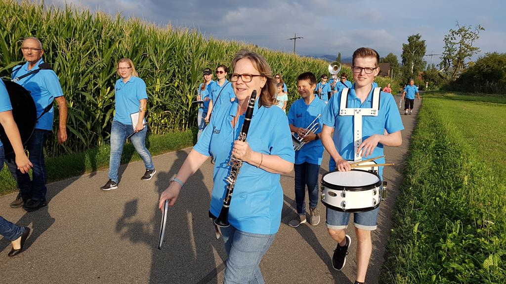 Die MGU marschiert mit ihren blauen Shirts an einem Maisfeld vorbei.
